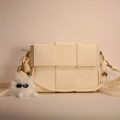 An ivory woven handbag with gold-tone hardware and an adjustable shoulder strap, displayed against a neutral background.